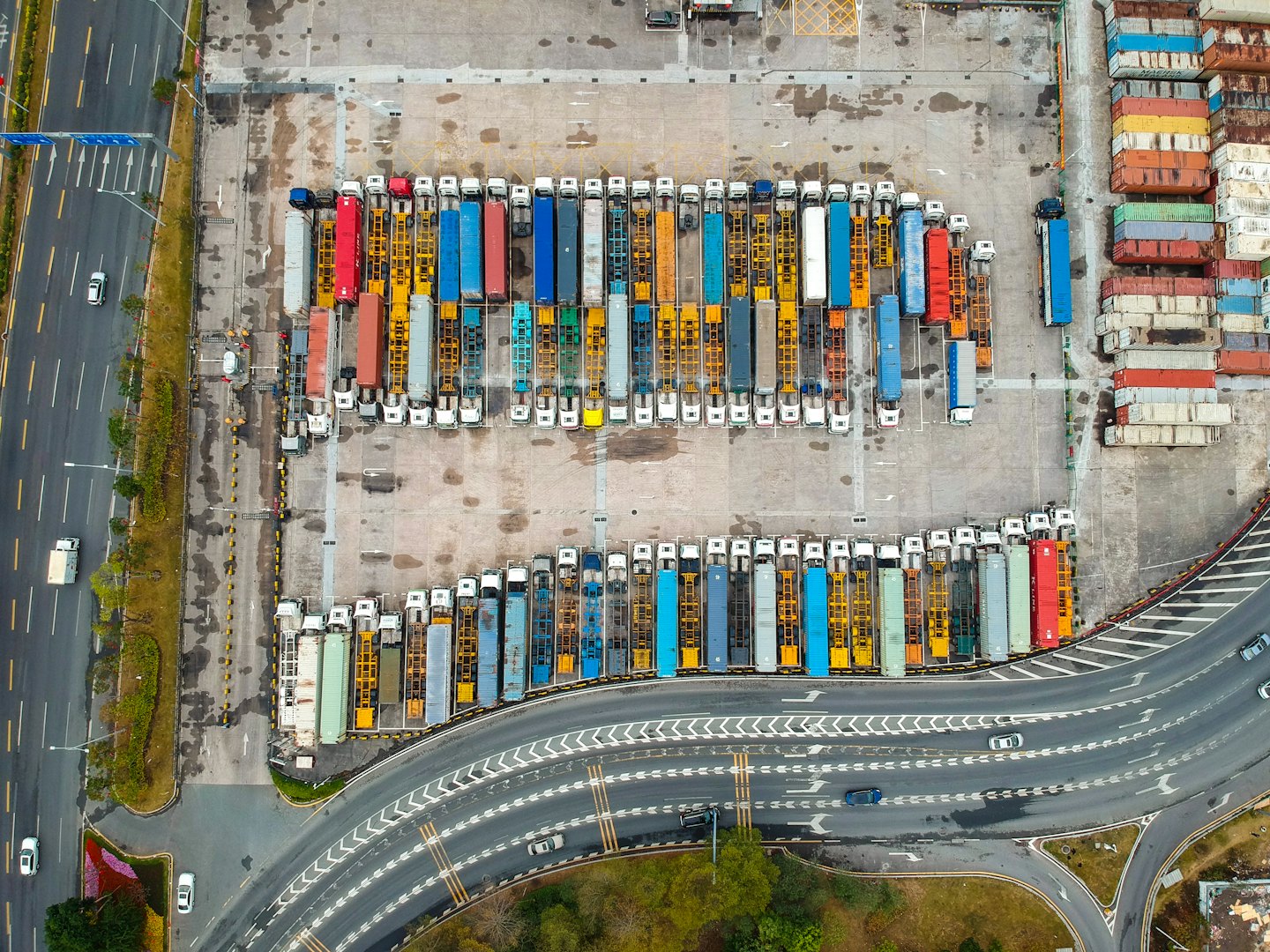 Viele Sattelzüge und gestapelte Schiffscontainer füllen einen großen Logistikhof.