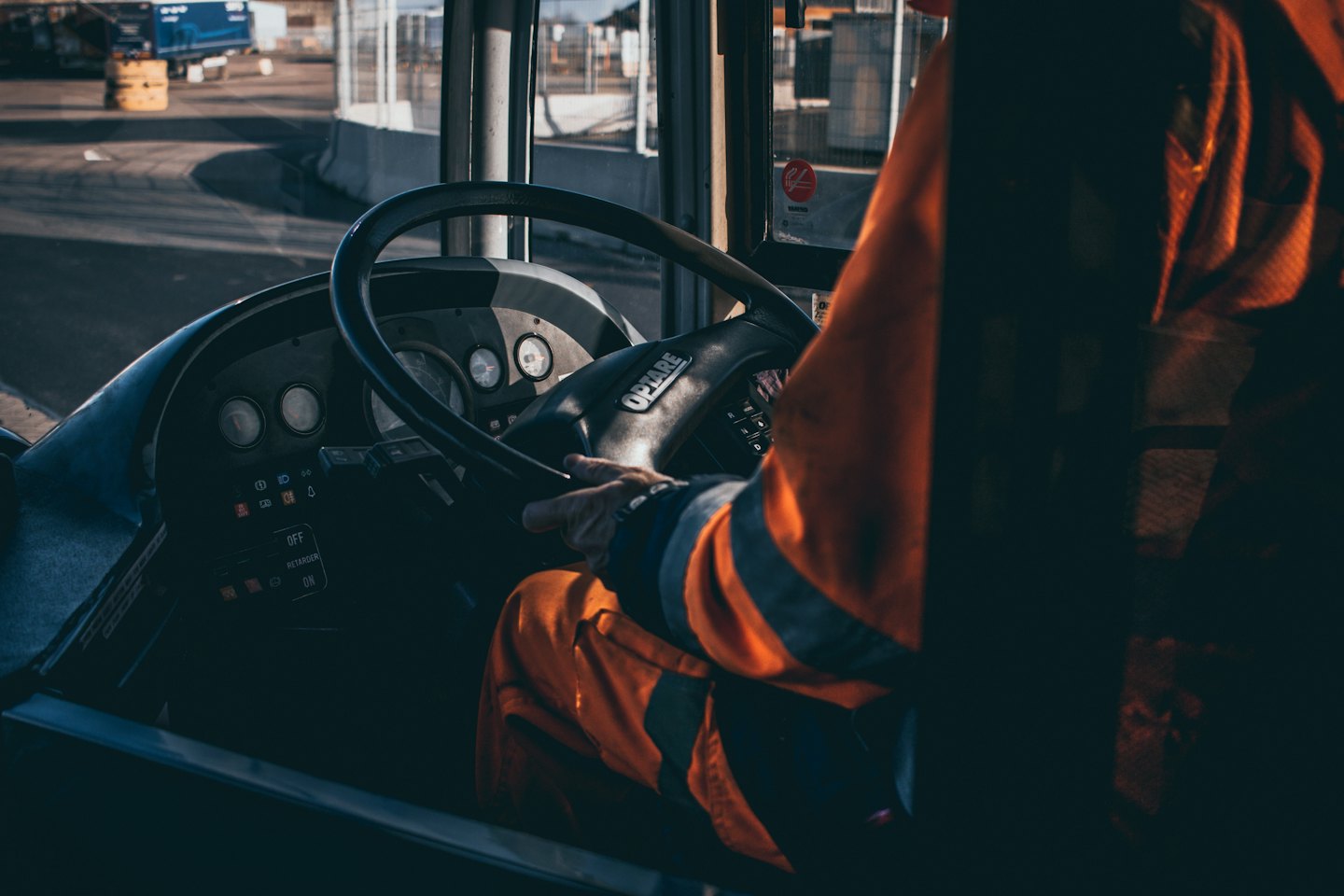 Fahrer in orangefarbener Uniform greift das Lenkrad eines großen Fahrzeugs.